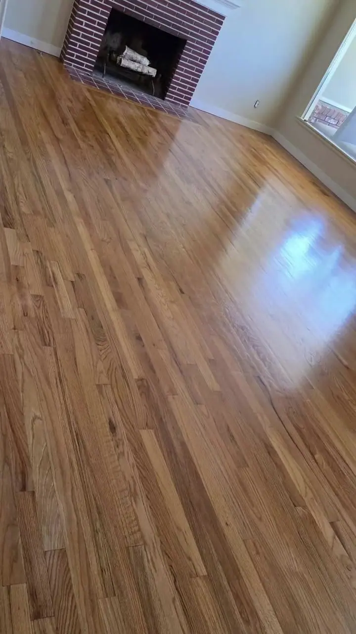 A refinished hardwood living room with a glossy floor, a stone fireplace, and a ceiling fan.