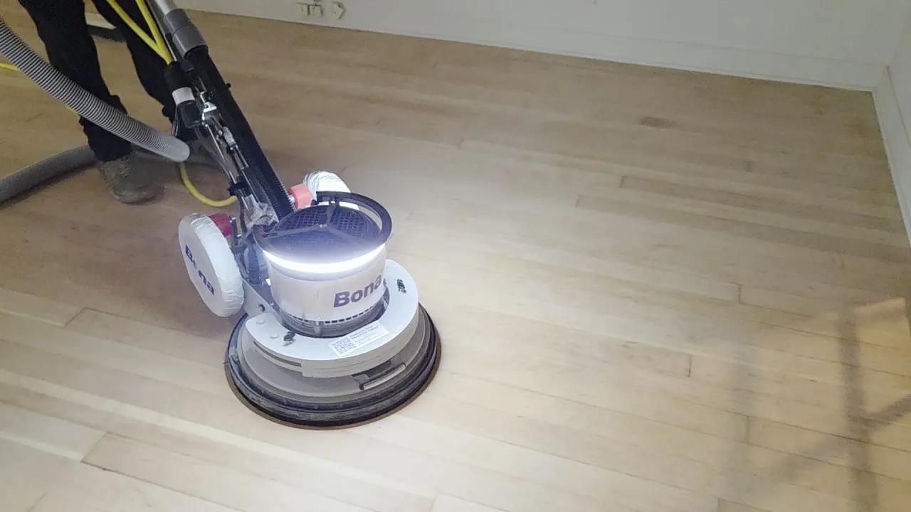 A floor sander working across the hardwood in an empty room.