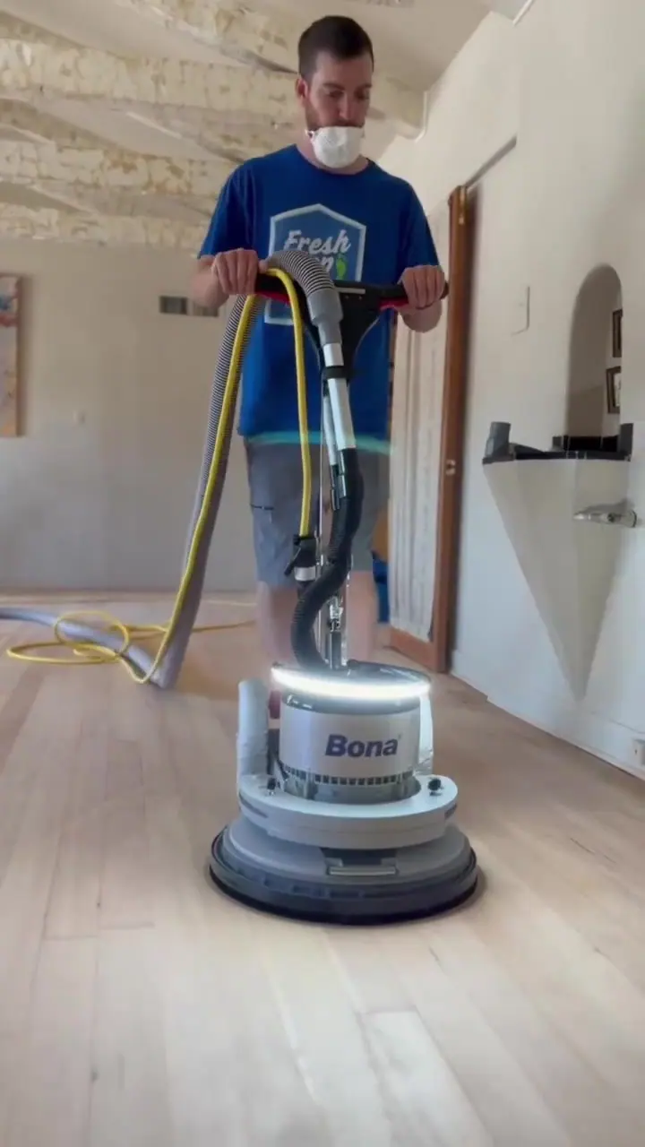 A technician in dark clothing guiding a floor sander across a hardwood floor.